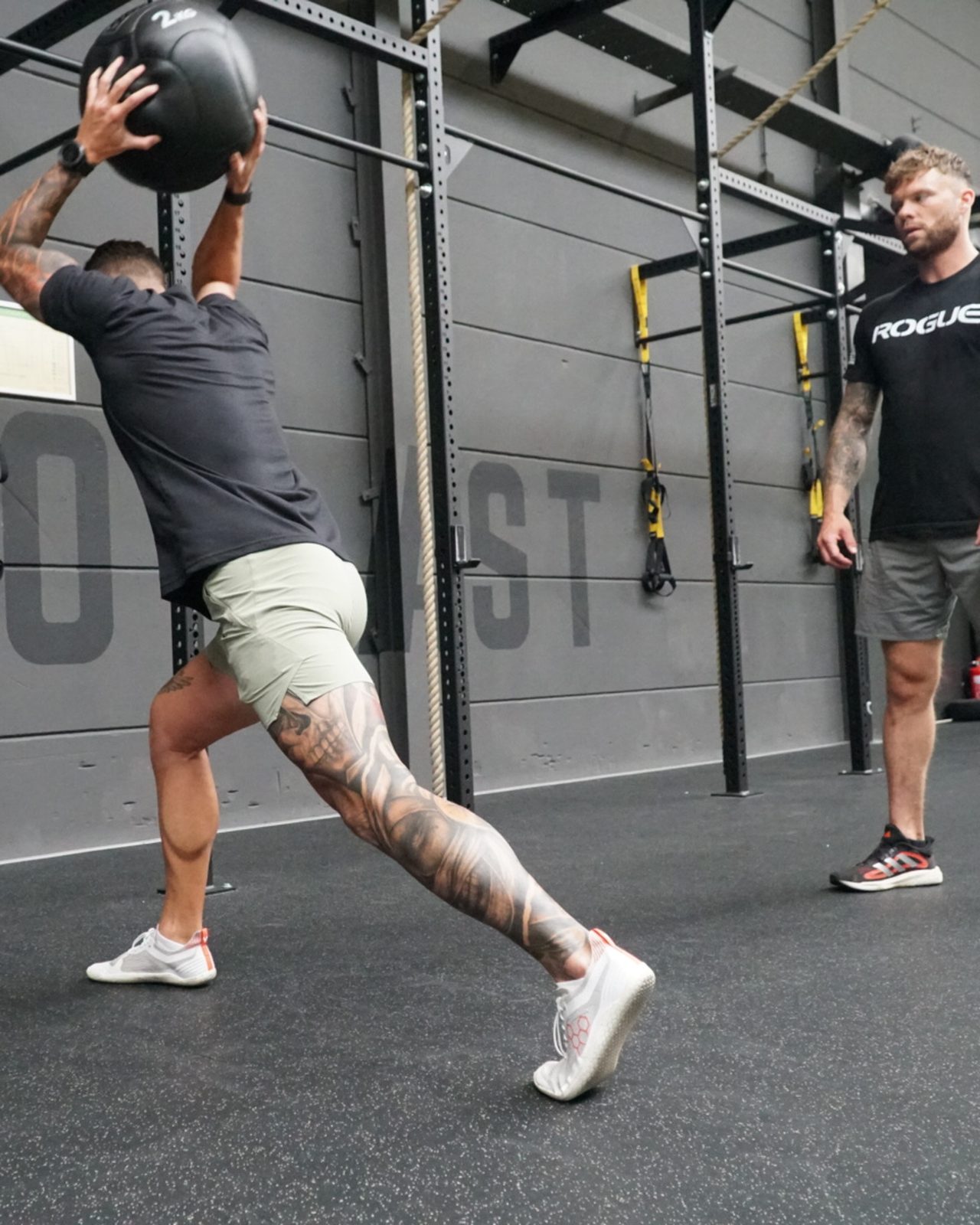 Sporter voert explosieve medicine-ball lunge uit terwijl de coach de uitvoering observeert